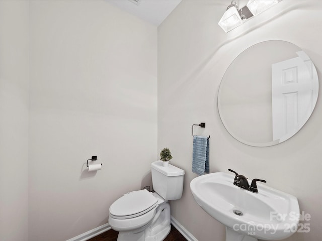 half bathroom with baseboards, toilet, and a sink
