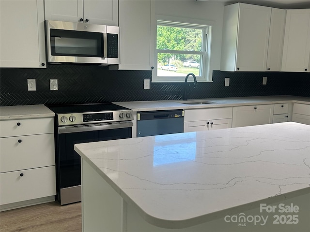 kitchen featuring appliances with stainless steel finishes, light stone counters, a sink, light wood-style flooring, and decorative backsplash