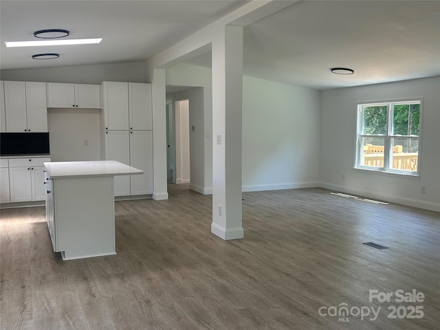 kitchen featuring baseboards, white cabinets, open floor plan, and lofted ceiling