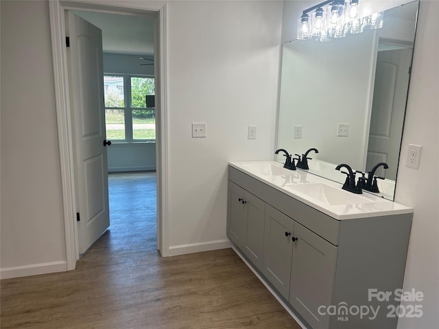 bathroom featuring baseboards, a sink, wood finished floors, and double vanity