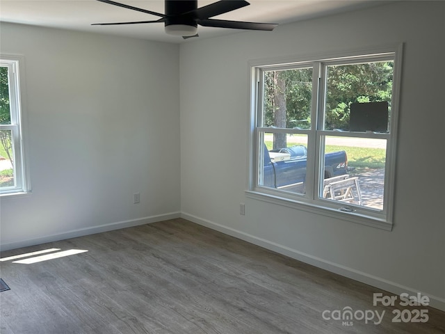 unfurnished room featuring a ceiling fan, baseboards, a wealth of natural light, and wood finished floors