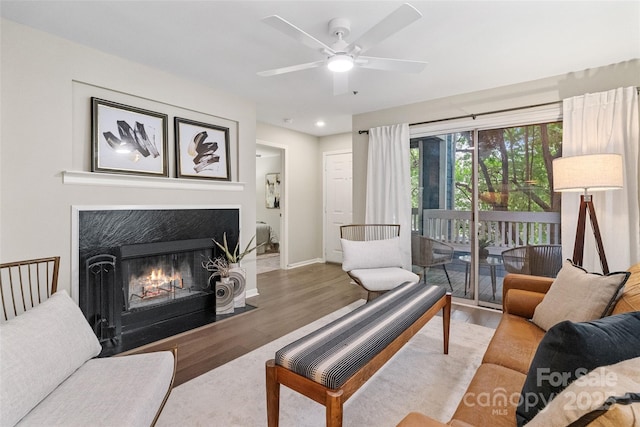 living room featuring wood finished floors, baseboards, ceiling fan, a fireplace with flush hearth, and recessed lighting