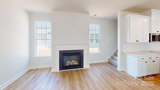 9612 Pointer Rd Unit 59, Huntersville, NC 28078 - unfurnished living room featuring stairs, light wood-style flooring, plenty of natural light, and a glass covered fireplace