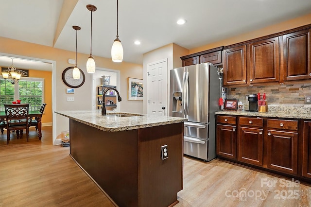 kitchen with decorative backsplash, light stone countertops, stainless steel fridge with ice dispenser, a sink, and light wood-style flooring