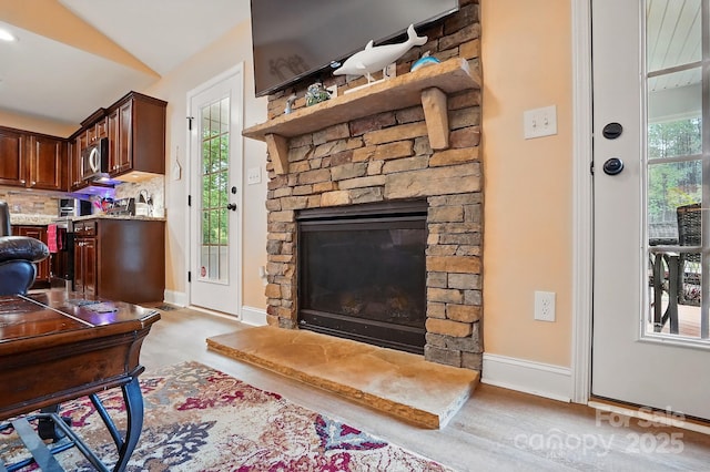 living area featuring baseboards, vaulted ceiling, wood finished floors, and a fireplace