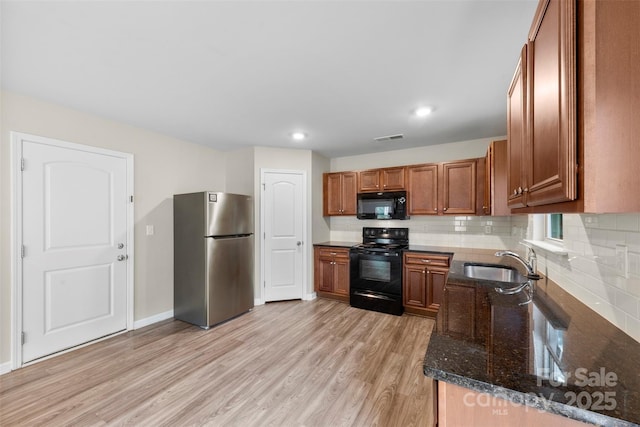 kitchen featuring black appliances, a sink, brown cabinets, light wood finished floors, and dark stone counters