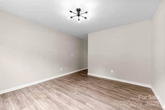spare room with a chandelier, wood finished floors, and baseboards