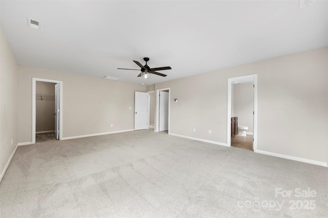 unfurnished bedroom with carpet floors, baseboards, a spacious closet, a ceiling fan, and ensuite bathroom