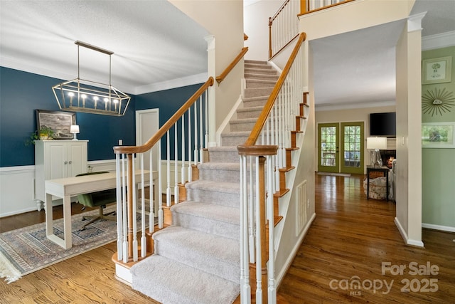 stairs with wood finished floors, crown molding, a chandelier, and wainscoting
