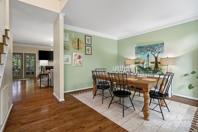 dining space with wood finished floors, crown molding, a lit fireplace, and baseboards