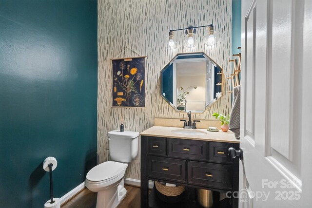 bathroom featuring vanity, toilet, baseboards, wallpapered walls, and wood finished floors
