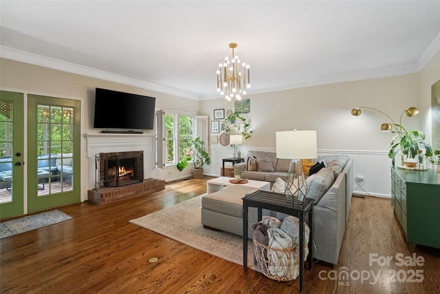 living room featuring wood finished floors, a notable chandelier, a fireplace, and crown molding