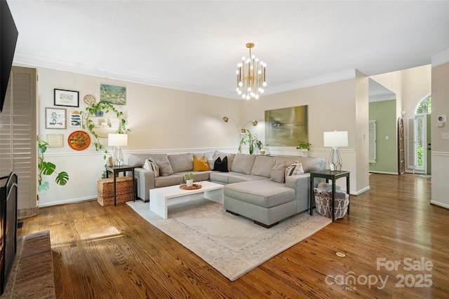 living room featuring wood finished floors, an inviting chandelier, ornamental molding, a brick fireplace, and baseboards