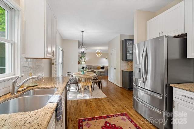 kitchen with white cabinetry, light wood-style flooring, a sink, stainless steel refrigerator with ice dispenser, and backsplash