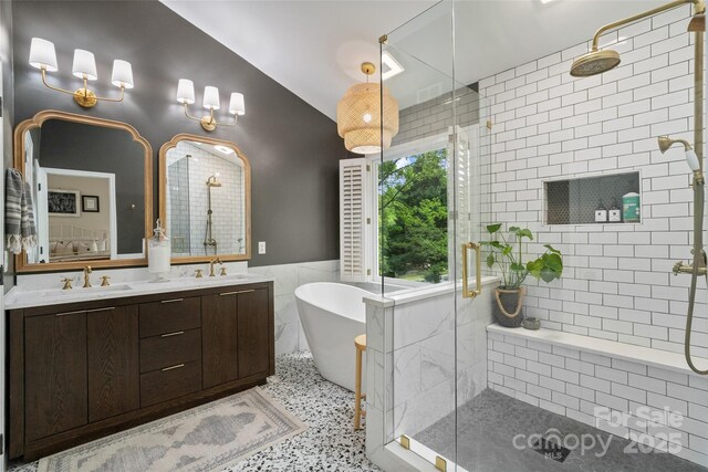 ensuite bathroom with a sink, a shower stall, a freestanding bath, and tile walls