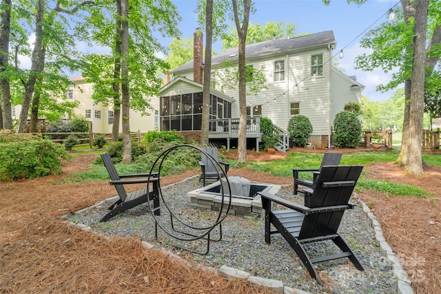 rear view of property featuring a sunroom, fence, a chimney, and an outdoor fire pit