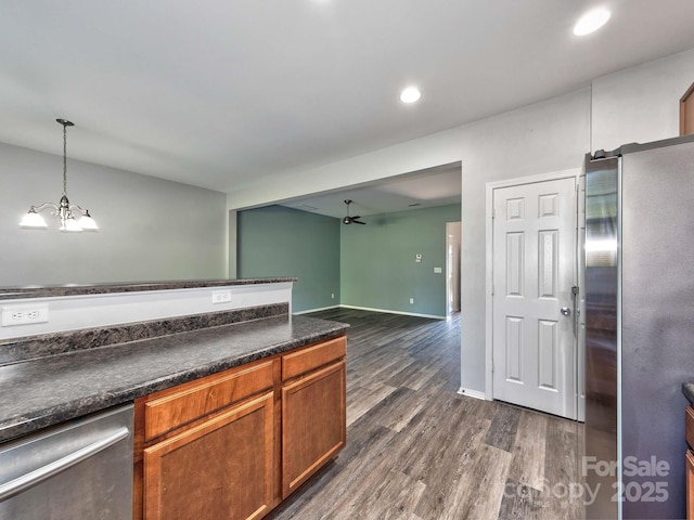 kitchen with dark wood finished floors, stainless steel appliances, brown cabinets, dark countertops, and ceiling fan with notable chandelier