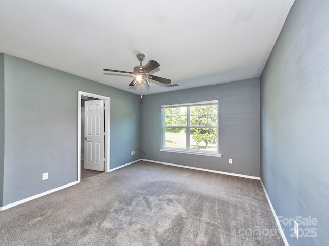 carpeted empty room with baseboards, visible vents, and a ceiling fan