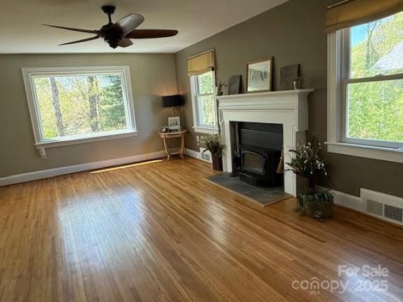 unfurnished living room featuring healthy amount of natural light, a wood stove, wood finished floors, and baseboards