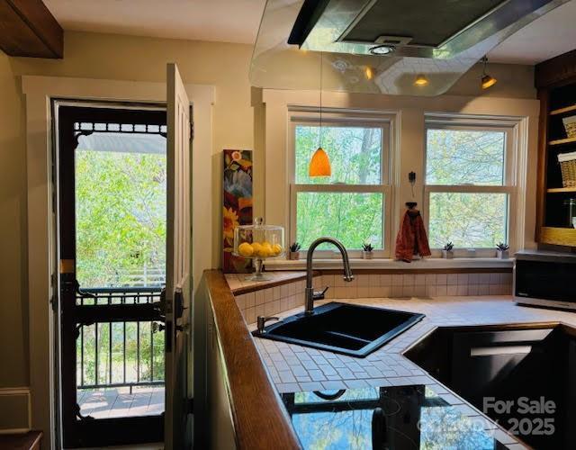 kitchen featuring stainless steel microwave, tile counters, a sink, and hanging light fixtures