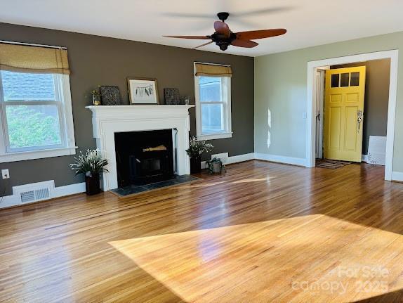 unfurnished living room featuring healthy amount of natural light, wood finished floors, a ceiling fan, and baseboards