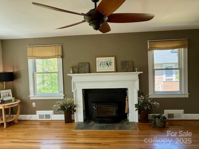 living room featuring wood finished floors, ceiling fan, a wood stove, and baseboards