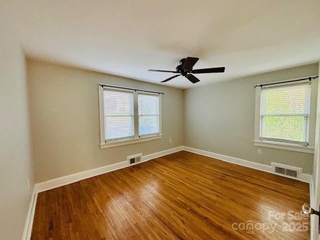 unfurnished room featuring healthy amount of natural light, wood finished floors, baseboards, and ceiling fan