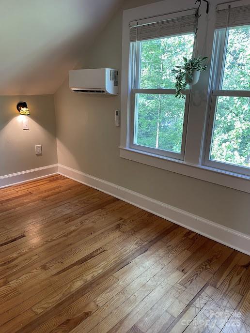 additional living space with lofted ceiling, a wall unit AC, baseboards, wood finished floors, and plenty of natural light