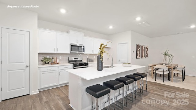 kitchen featuring a sink, stainless steel appliances, decorative backsplash, a breakfast bar area, and light wood-style flooring