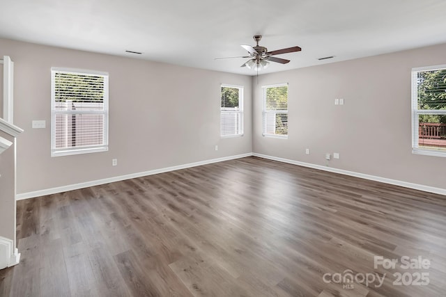 empty room with baseboards, ceiling fan, wood finished floors, and visible vents