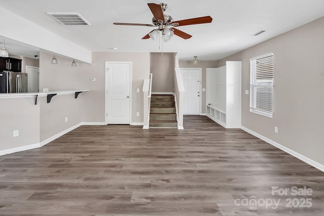unfurnished living room with visible vents, a ceiling fan, wood finished floors, and stairway