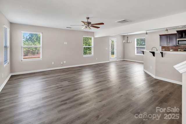 unfurnished living room with baseboards, a ceiling fan, dark wood-style floors, and visible vents