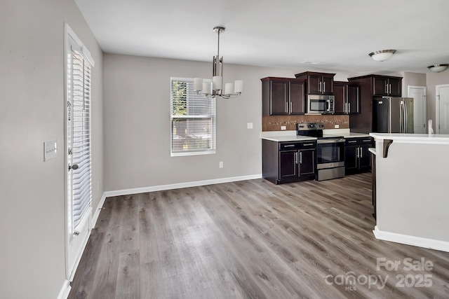 kitchen featuring appliances with stainless steel finishes, light countertops, baseboards, an inviting chandelier, and light wood-style flooring