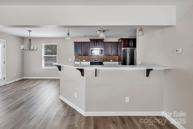 kitchen with baseboards, light wood finished floors, a breakfast bar area, and stainless steel appliances
