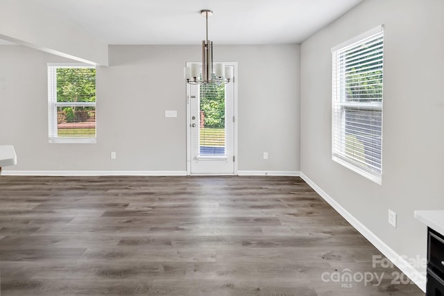 unfurnished dining area featuring plenty of natural light, baseboards, wood finished floors, and an inviting chandelier