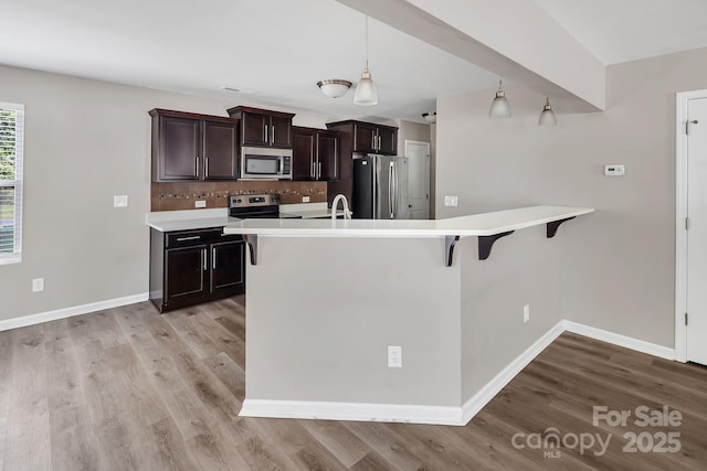kitchen with light countertops, stainless steel appliances, light wood-style flooring, and a kitchen bar