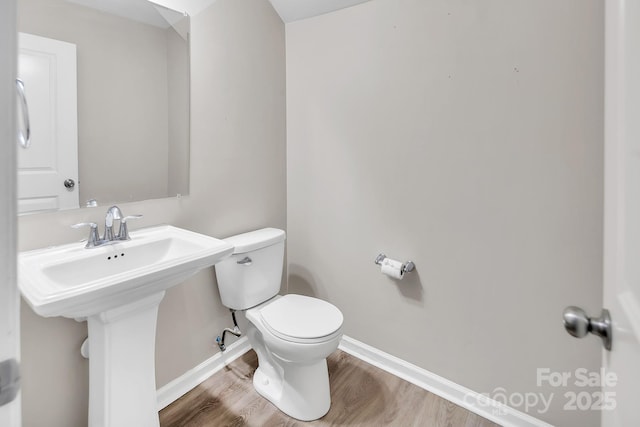 bathroom featuring baseboards, wood finished floors, and toilet