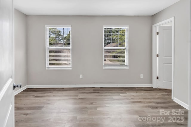 spare room with baseboards, wood finished floors, and a healthy amount of sunlight