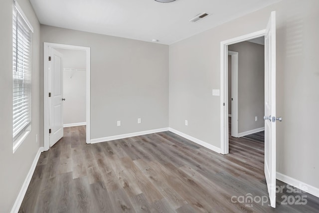 unfurnished bedroom featuring baseboards, a walk in closet, visible vents, and wood finished floors
