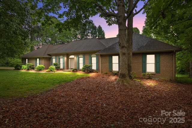 ranch-style home featuring a lawn, roof with shingles, and brick siding