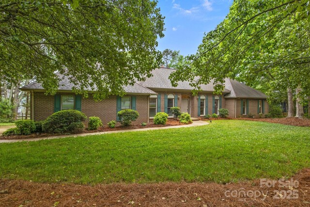 ranch-style house with brick siding, a front yard, and roof with shingles