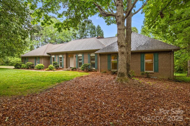 single story home featuring brick siding, a front yard, and roof with shingles