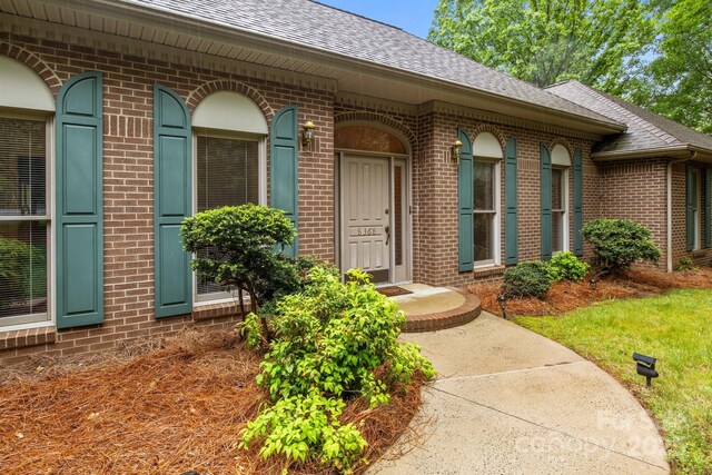 doorway to property with roof with shingles and brick siding