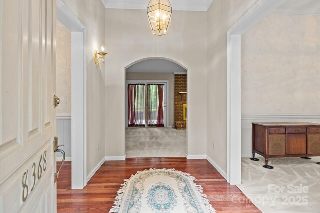 entrance foyer with crown molding, arched walkways, wood finished floors, and a chandelier