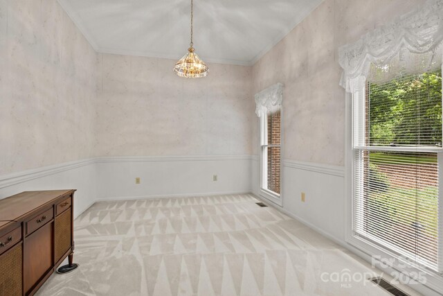 unfurnished dining area featuring crown molding, a wainscoted wall, visible vents, and light carpet