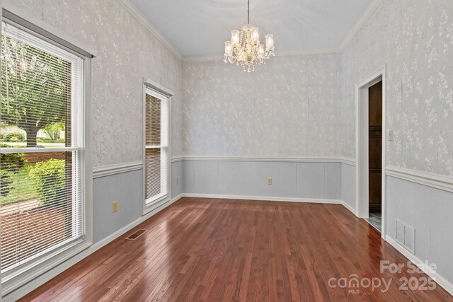unfurnished dining area with visible vents, ornamental molding, wood finished floors, and an inviting chandelier