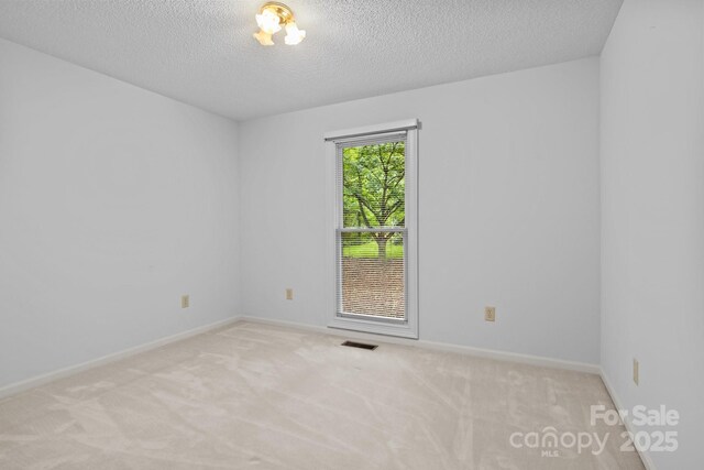 carpeted spare room featuring a textured ceiling, visible vents, and baseboards
