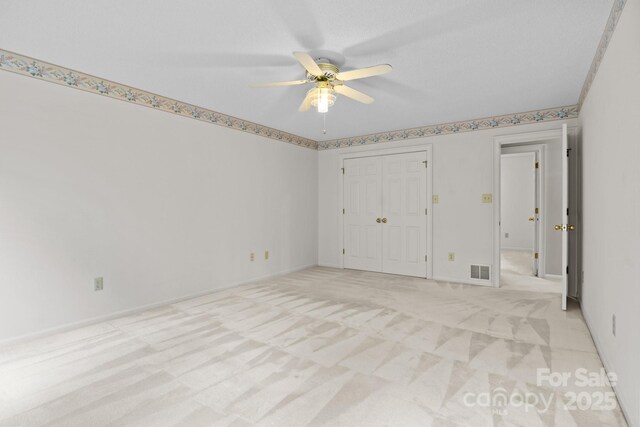 unfurnished bedroom with ceiling fan, light colored carpet, visible vents, baseboards, and a closet