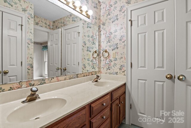 full bathroom featuring toilet, double vanity, wallpapered walls, and a sink