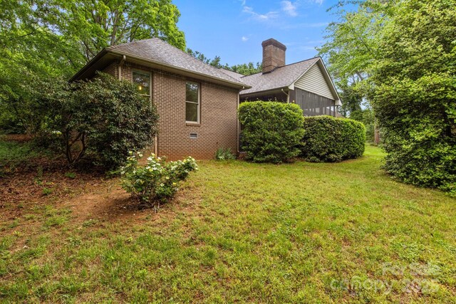 view of property exterior with brick siding, a shingled roof, a yard, and a chimney